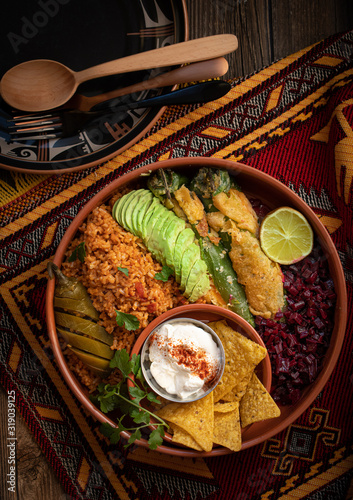 Vegetarian Mexican bowl containing rice, stuffed  chilies, beet side, avocado, sour cream and pickles