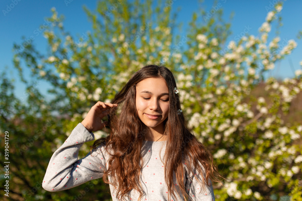 Naklejka premium Portrait of a young beautiful teenager girl in a blooming spring green garden