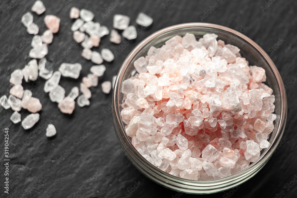 Spilled salt near a saucer full of Himalayan salt on a black slate board