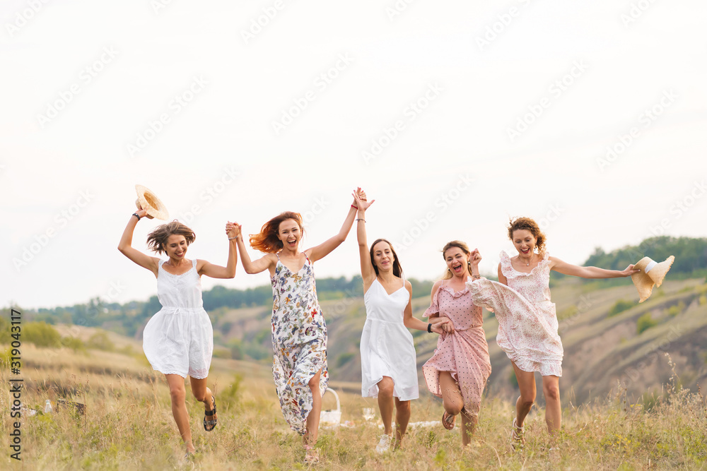 The company of cheerful female friends have a great time together on a picnic in a picturesque place overlooking the green hills. Girls in white dresses dancing in the field The company of cheerful female friends have a great time together on a picnic in a picturesque place overlooking the green hills. Girls in white dresses dancing in the field
