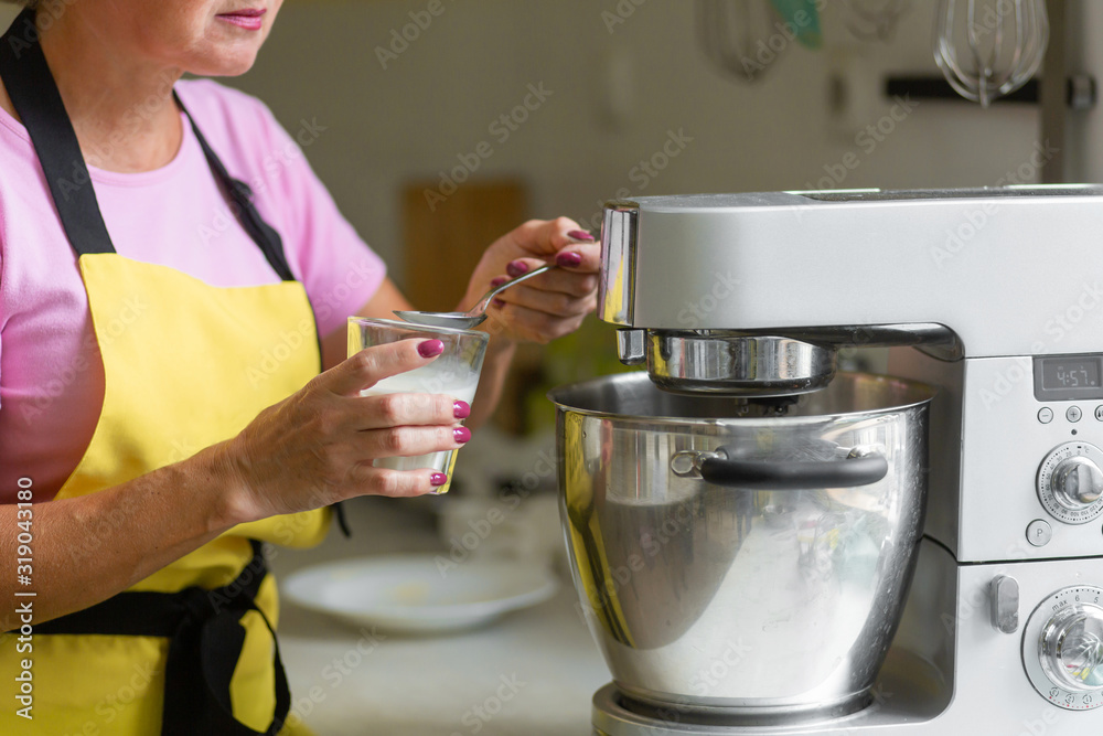 Woman professional pastry chef preparing a dessert. Adds ingredients and mixes the dough in a mixer