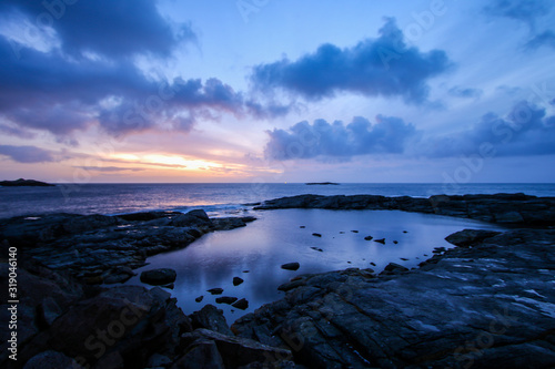 Rocky coastline with a natural pool in the small fishing village of A  Moskenes  at the end of the road of the Lofoten islands archipelago in northern Norway - Red rorbuer on stilts in winter at dawn