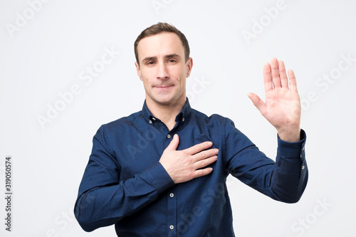 Obraz na płótnie Sincere happy man raising palm and holding hand on chest, promising to me honest