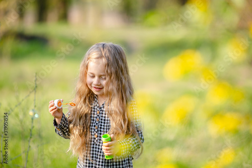 Cute little blonde girl blowing soap bubbles having fun in the spring park.