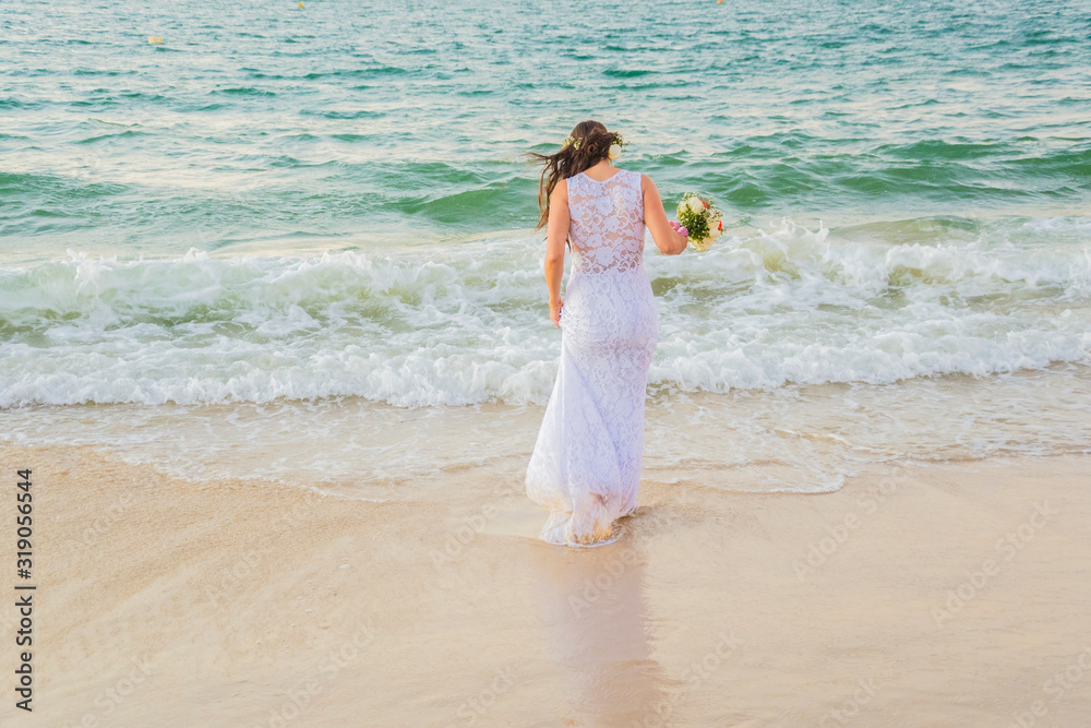 Back view of bride entering the sea with wedding dress and bouquet in hand. Back view of bride entering the sea with wedding dress and bouquet in hand.