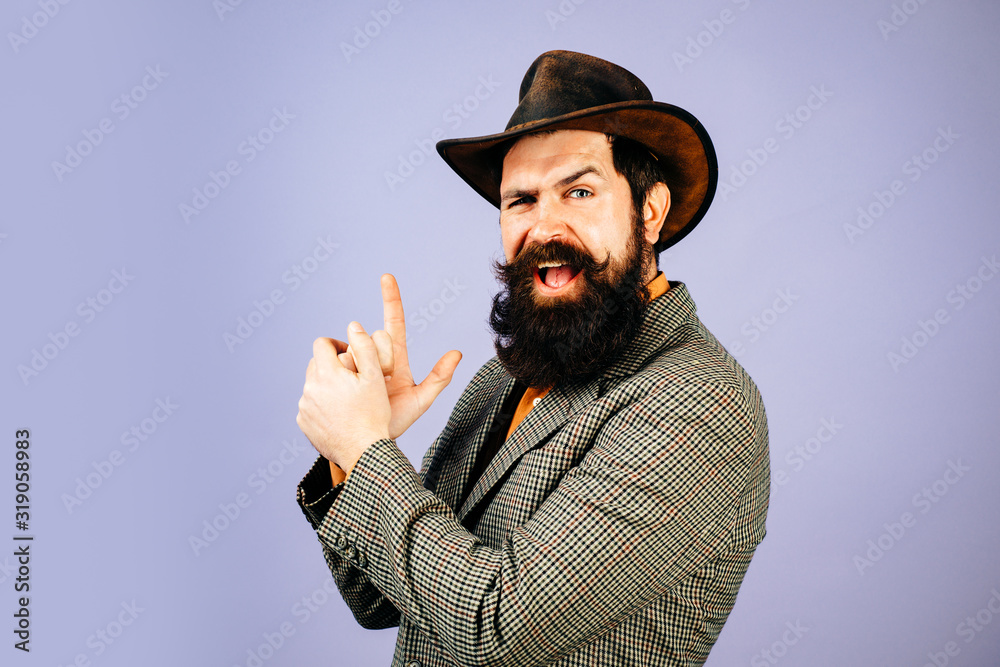 Young handsome bearded carefree funny man in suit with fingers like guns. Close up photo of fine brunet in hat with imagine gun in hands on isolated background. Young handsome bearded carefree funny man in suit with fingers like guns. Close up photo of fine brunet in hat with imagine gun in hands on isolated background.