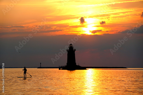 Silhouette of a light house and a man on a paddle board during sunset at Cape Henlopen State Park, Lewes, Delaware, U.S.A
