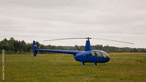 Blue private helicopter on the grass against a cloudy sky