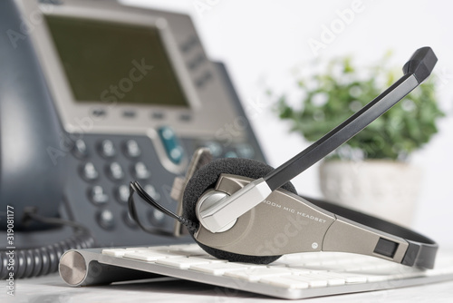 Phone and headphones on a PC keyboard, work in a call center, support service on a light office background