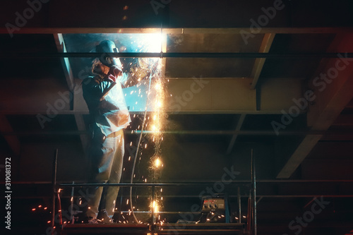 Photography Profesional welder in protective uniform and mask welding metal construction in the industrial object