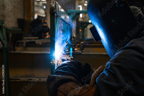 Man with mask welding steel between sparks in a workshop