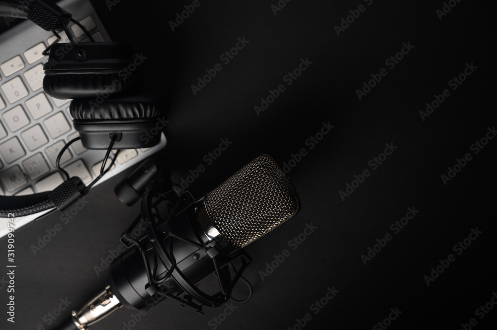 Flat lay, Studio microphone with professional headphones on a PC keyboard. Black on a black background. Podcasts, radio, streams, blogging, working with sound, recording tracks