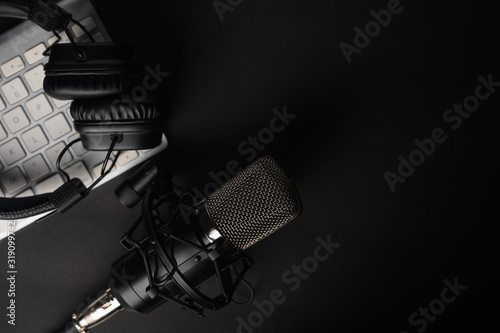Flat lay, Studio microphone with professional headphones on a PC keyboard. Black on a black background. Podcasts, radio, streams, blogging, working with sound, recording tracks
