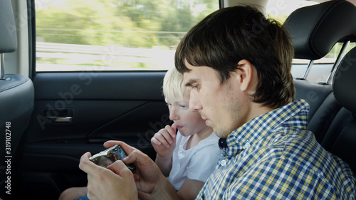 Father with son sitting in car seat and playing on smart phone while having car ride in backseat photo