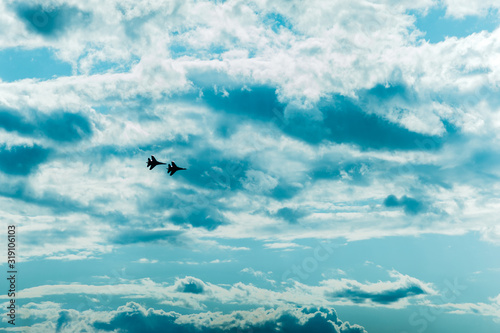 two fighter jets fly in a clear blue sky with clouds one way photo