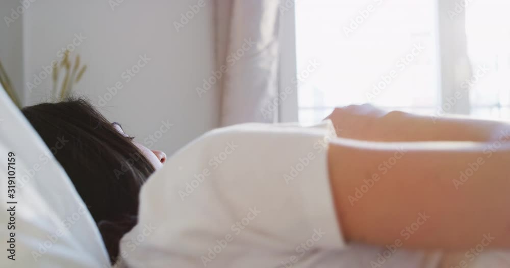 A healthy young woman is waking up after sleeping well with a sun beams in her bedroom in a morning. Shot in 8K. Concept of wellbeing, healthcare, lifestyle,bedding, happiness