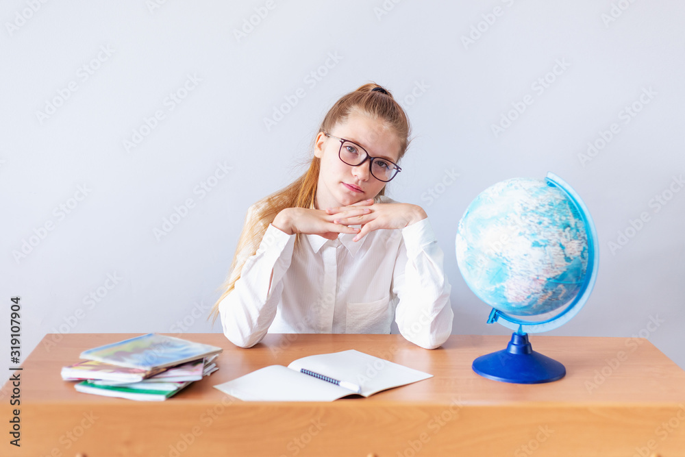 portrait of a pensive girl with glasses. she sits at the table, dreams of traveling, and looks at the globe portrait of a pensive girl with glasses. she sits at the table, dreams of traveling, and looks at the globe