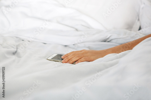 Close-up hand holds the phone in bed. The girl fell asleep with a phone in her hand and she is addicted. Or a person reaches for a mobile phone to turn off the alarm.