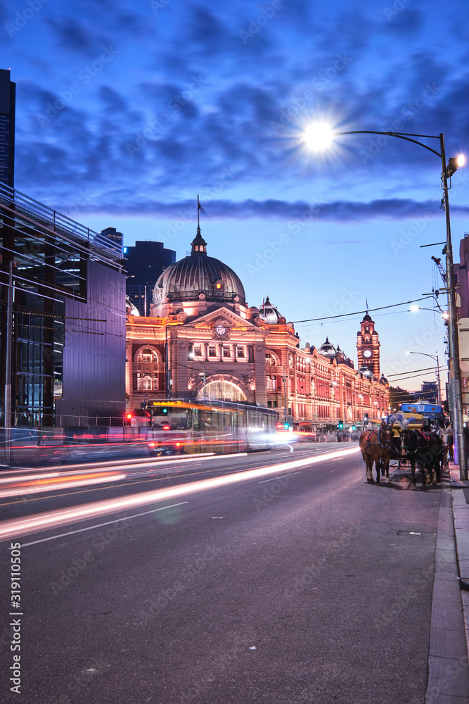 Fototapeta premium Melbourne, Victoria / Australia - January 26 2020: Flinders Street Station and church with light trails, car trails, trams, cars and tourists at blue hour