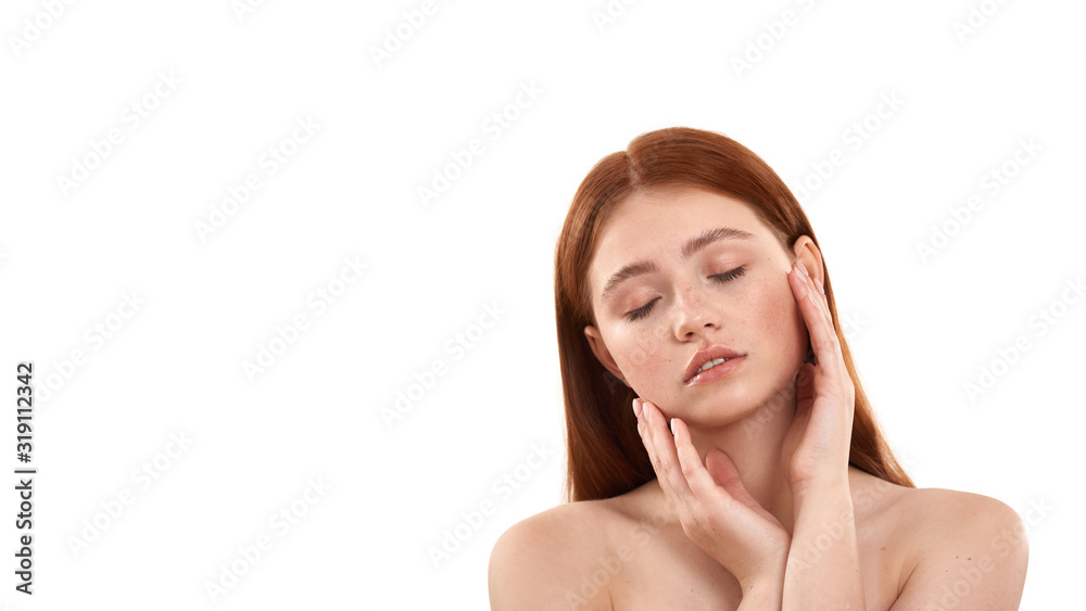 Enjoying her soft skin. Young sensual red-haired girl keeping eyes closed and touching her face while standing against white background. Beauty portrait Enjoying her soft skin. Young sensual red-haired girl keeping eyes closed and touching her face while standing against white background. Beauty portrait