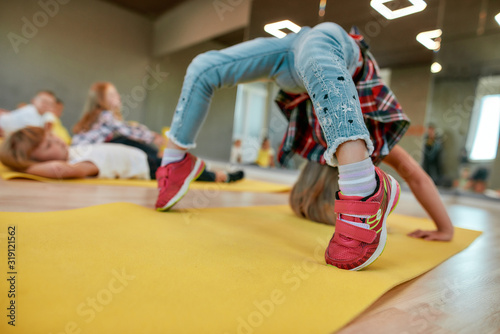 Staying flexible. Little girl making backbend on yoga mat in the dance studio. Group of children doing gymnastic exercises photo