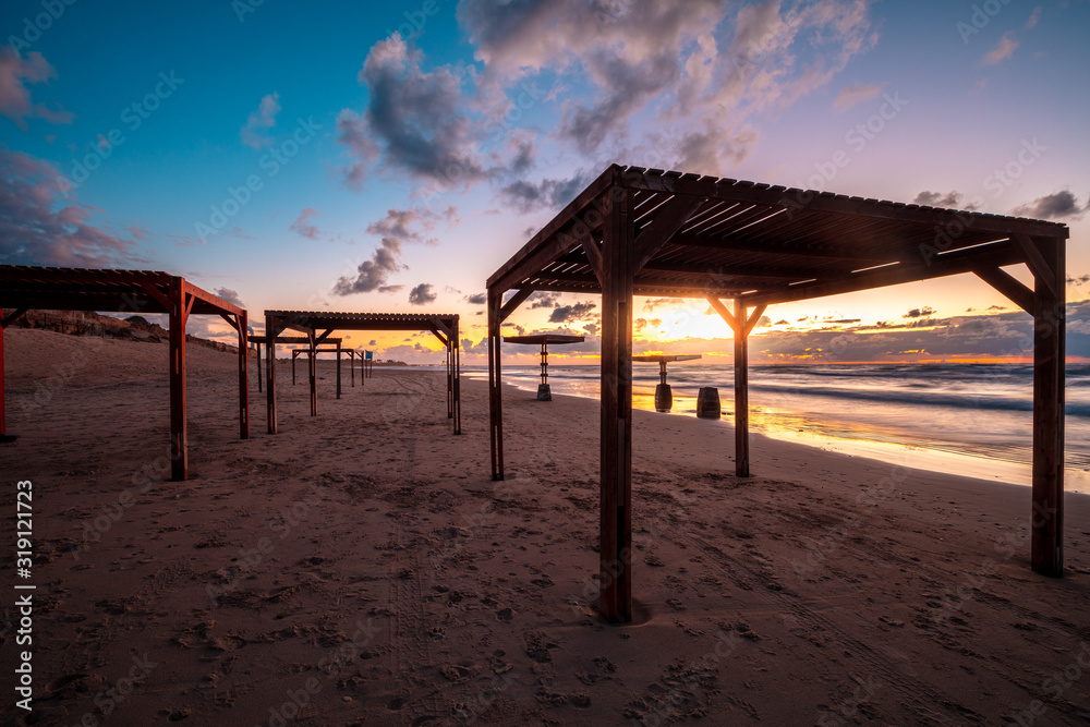 Sunset over the beach with sunshade umbrellas. Evening on the empty beach. Caesarea, Israel