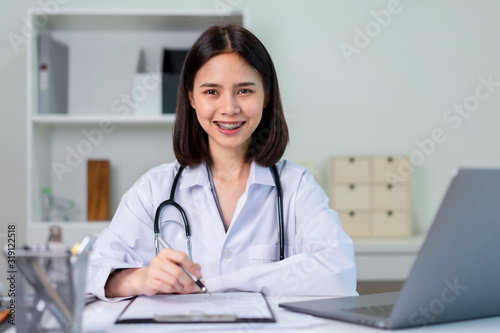 Smiling Asian doctor is wearing a stethoscope in the office.