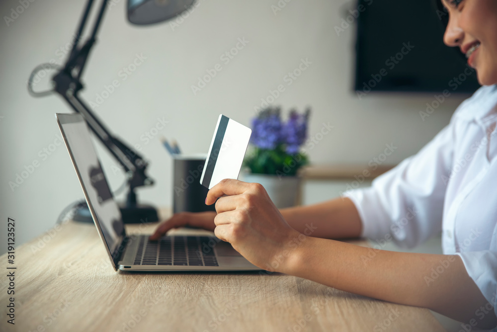 Asian woman holding credit cart and using laptop to shopping online.Shopaholic girl selecting products to cart in online website And pay via internet banking. Asian woman holding credit cart and using laptop to shopping online.Shopaholic girl selecting products to cart in online website And pay via internet banking.