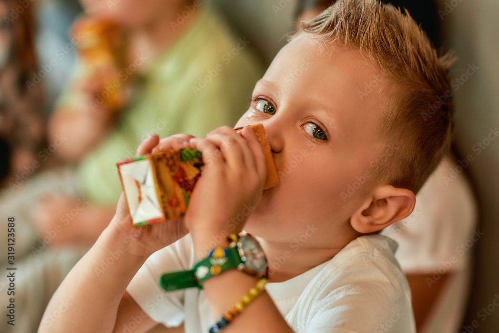 Energy drink. Portrait of a cute and stylish little boy in white t-shirt drinking a juice and looking at camera. Relaxing after intensive choreography class in the dance studio Energy drink. Portrait of a cute and stylish little boy in white t-shirt drinking a juice and looking at camera. Relaxing after intensive choreography class in the dance studio
