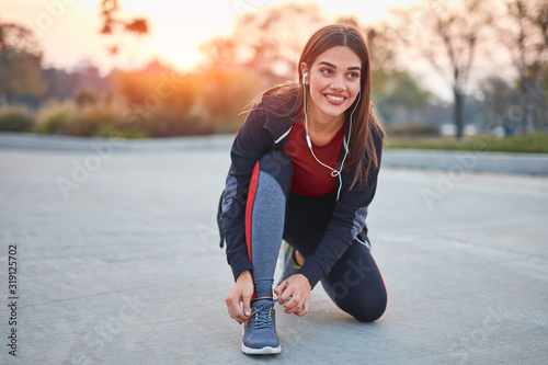 Young modern woman tying running shoes in urban park.