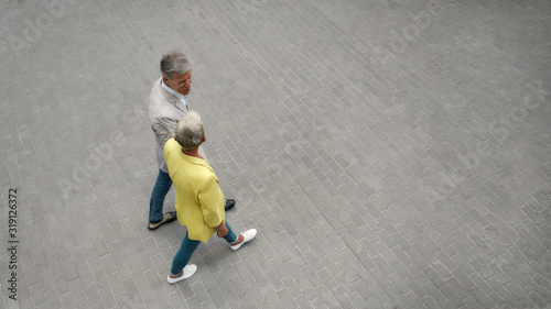 Top view of stylish mature couple holding hands and walking together through the city street
