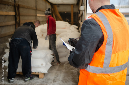 Canvas Print a manager in a protective helmet and overalls controls the unloading and records the number of bags of flour