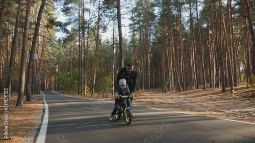 Wallpaper Mural Dad teaches little son to ride a balance bike on the road through the pine park Torontodigital.ca