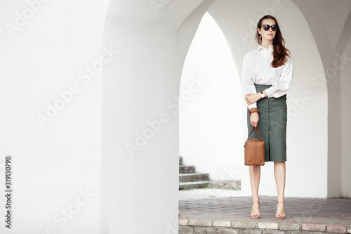 Young brunette business woman walking in city street. Stylish fashion model in sunglasses. Outdoor portrait of beautiful elegant woman 