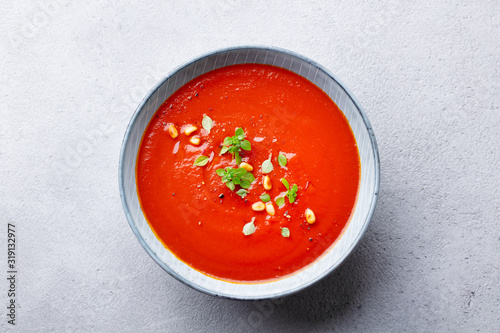 Tomato soup with fresh herbs and pine nuts in a bowl. Grey stone background. Top view.