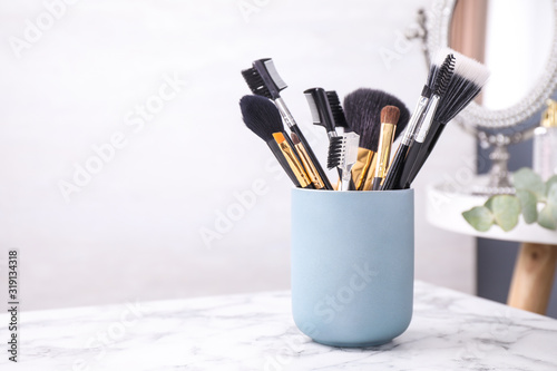 Set of professional makeup brushes in holder on white marble table. Space for text