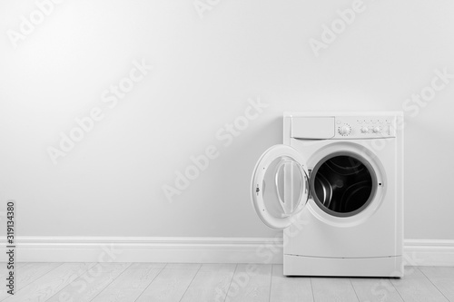 Modern washing machine near white wall, space for text. Laundry day