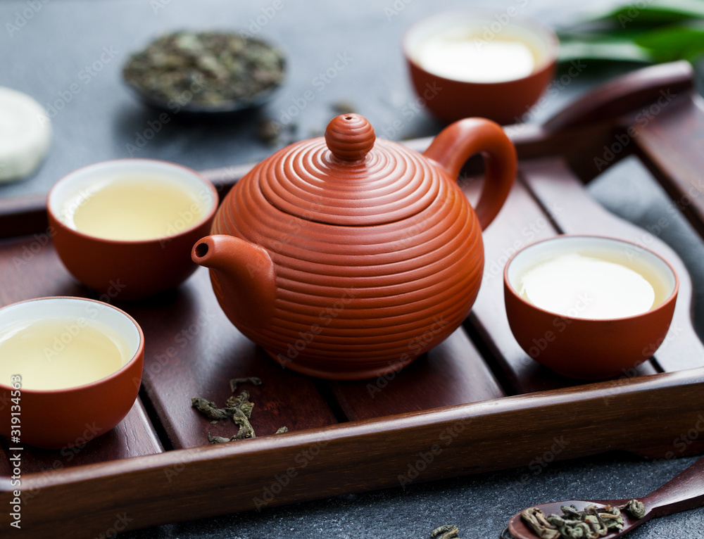 Fototapeta premium Green tea in tea pot and bowls, cups on wooden tray. Close up.