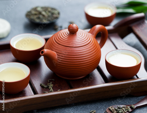 Green tea in tea pot and bowls, cups on wooden tray. Close up.