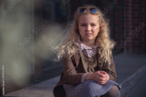 curly-haired blonde girl against the background of a brick wall and a glass window