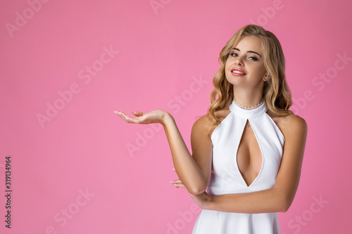 smiling young beautiful sexy woman in white dress showing copyspace pointing on pink background.