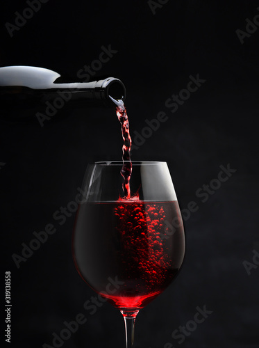 glass goblet with red wine pouring from bottle for romantic evening closeup on black background isolated