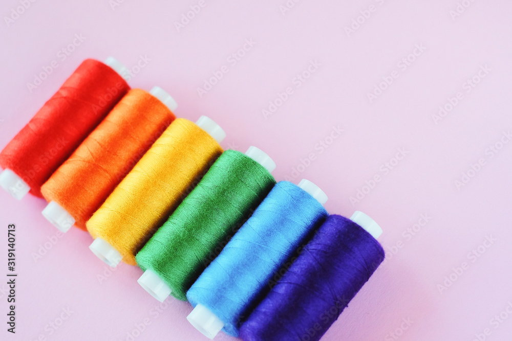 LGBT flag colors creative concept. Rainbow color sewing treads on the pink pastel  background.