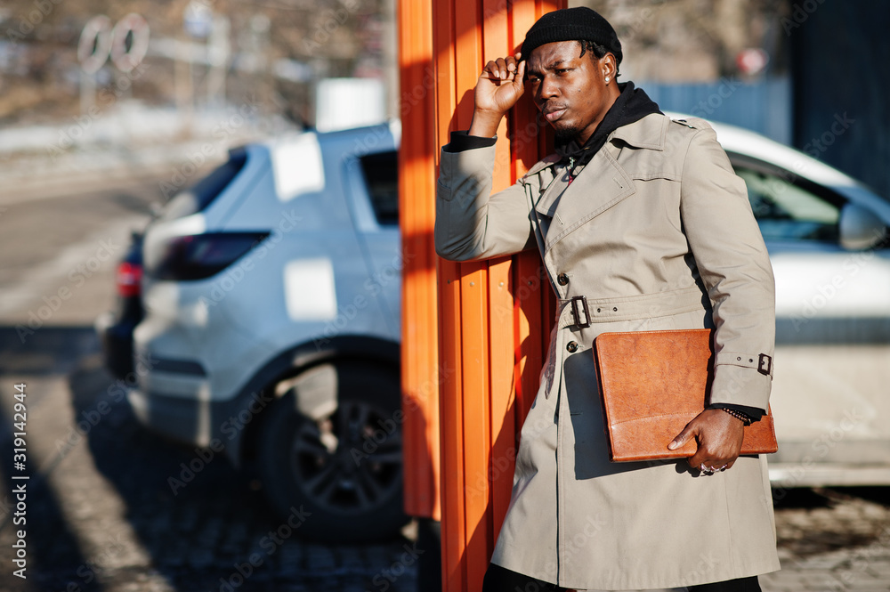 Handsome african american man posing outside in black hat and beige coat with folder in hand. Handsome african american man posing outside in black hat and beige coat with folder in hand.