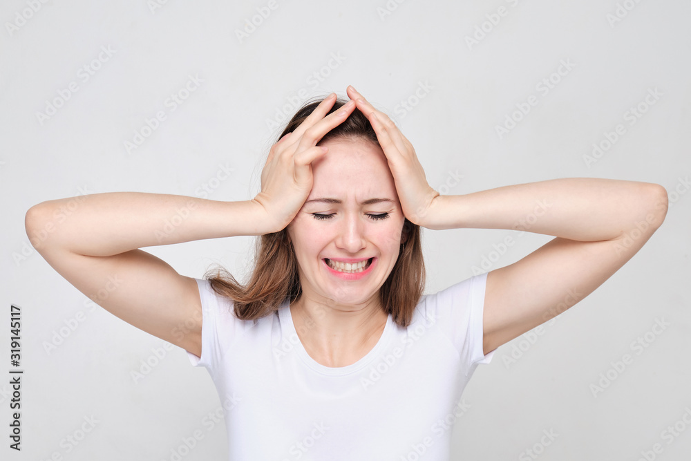A girl in a white T-shirt holds head with her hands. The concept of stress and problems. A girl in a white T-shirt holds head with her hands. The concept of stress and problems.