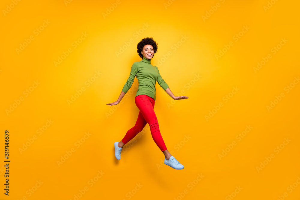 Full length body size turned photo of curly wavy brunette hair girl running jumping in red trousers white footwear isolated vivid color background