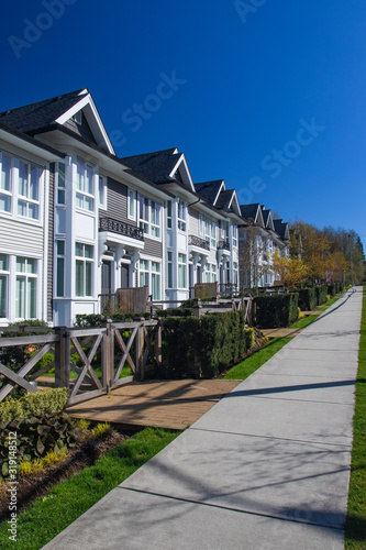 Row of new townhomes in a sidewalk neighborhood. On a sunny day in spring against bright blue sky. © Roman