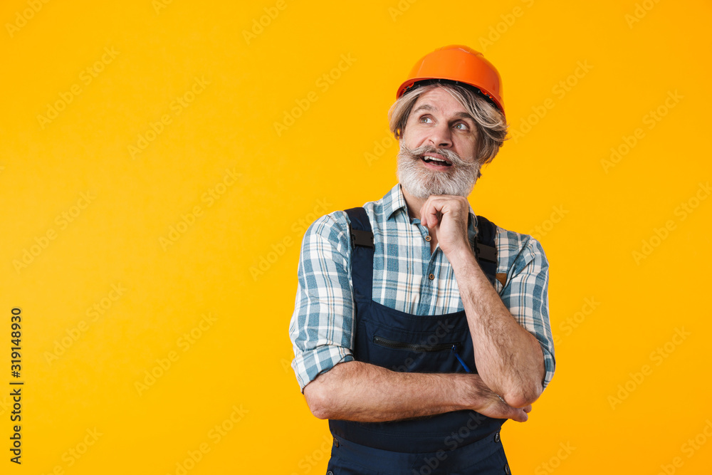 Thinking elderly grey-haired man builder in helmet