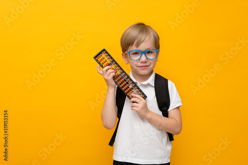 Cute little school boy in glasses holding abacus on yellow background. Mental arithmetic