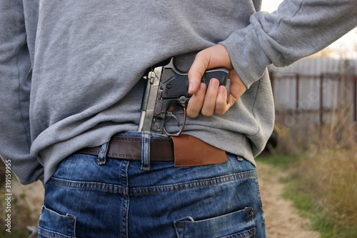 A man in jeans and a sweatshirt holds a gun in his hand from the back.